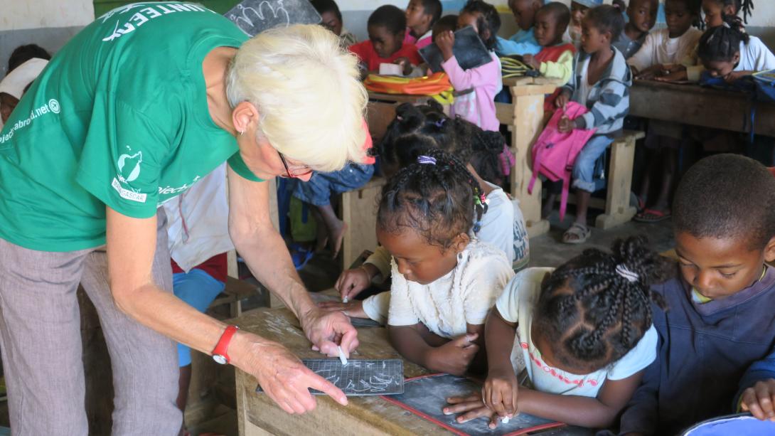An older female volunteer works with children in Africa as part of her retirement. On a volunteer abroad program for older adults, a woman works with school children in Madagascar.